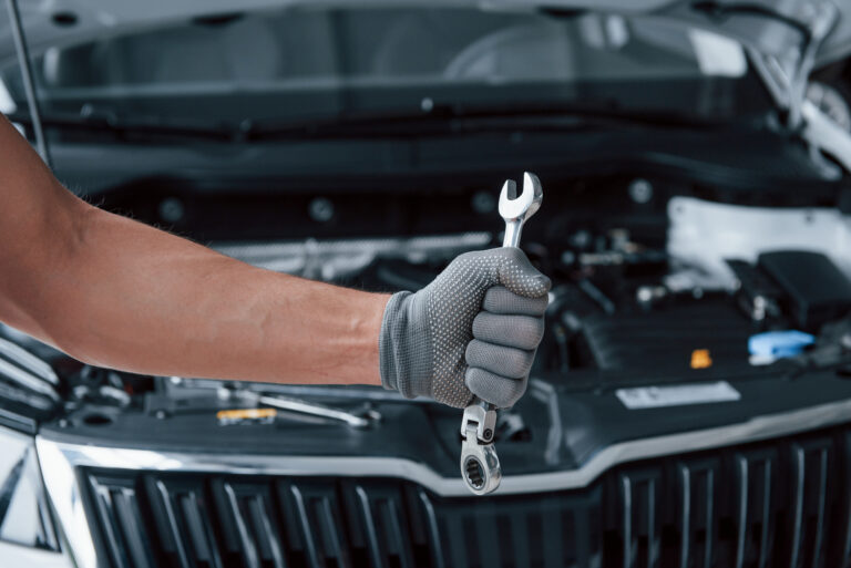 blurred background man s hand glove holds wrench front broken automobile